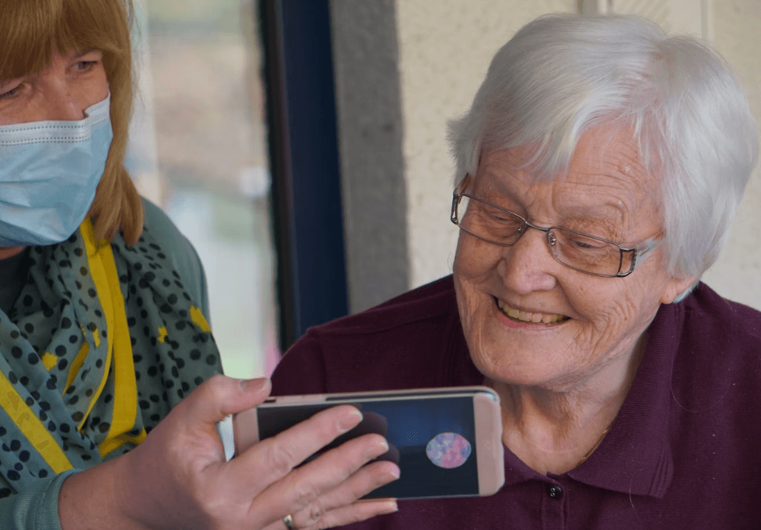 older woman being shown a video on a mobile phone by carer