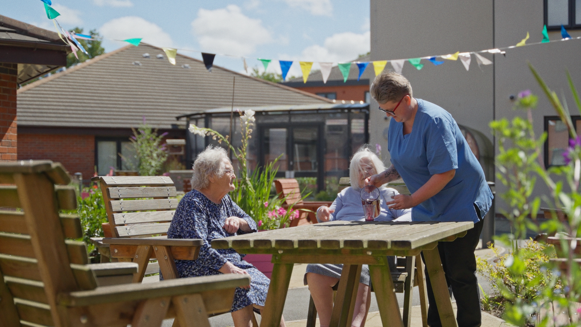 Residents at Chirk Court enjoying the outside seating area with staff member pouring a drink.