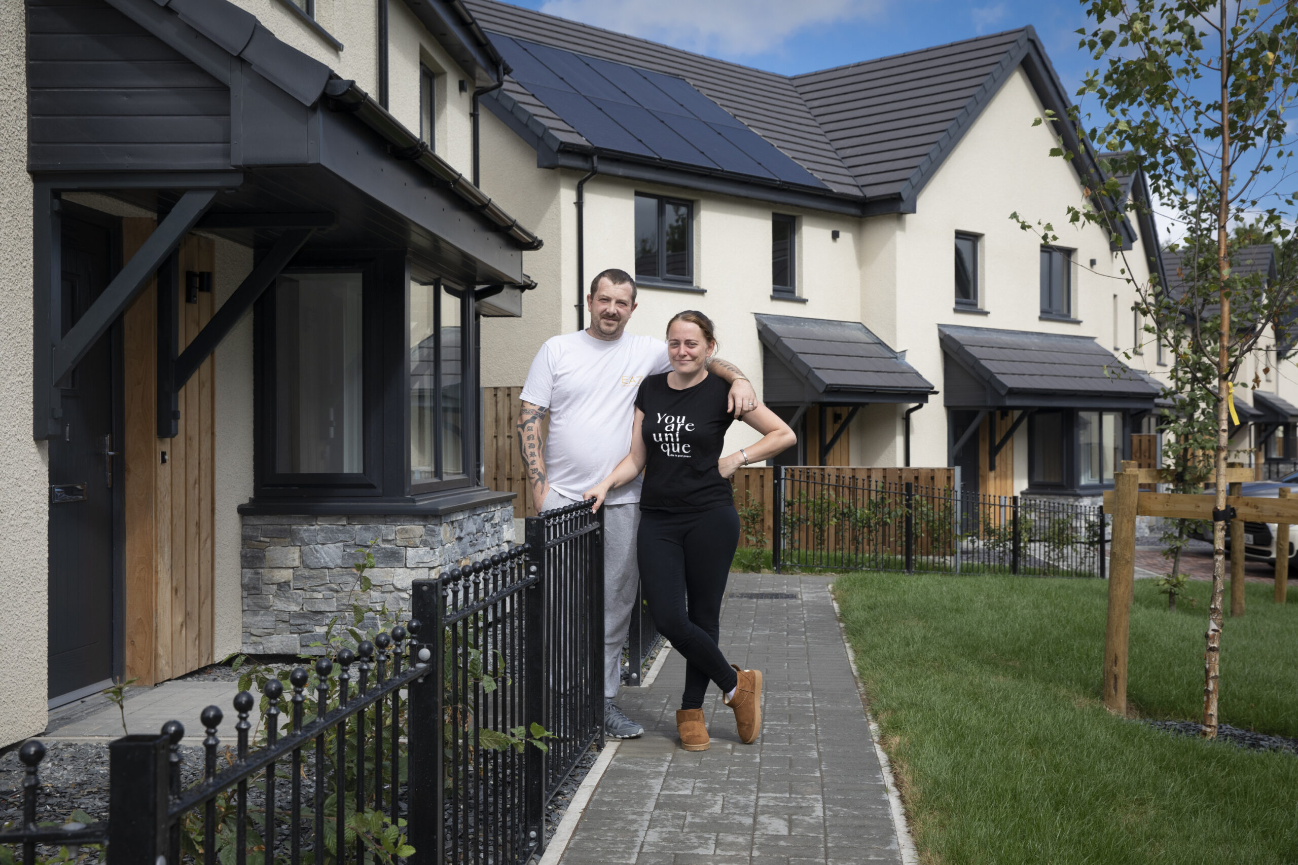 A couple outside their home smile at the camera.