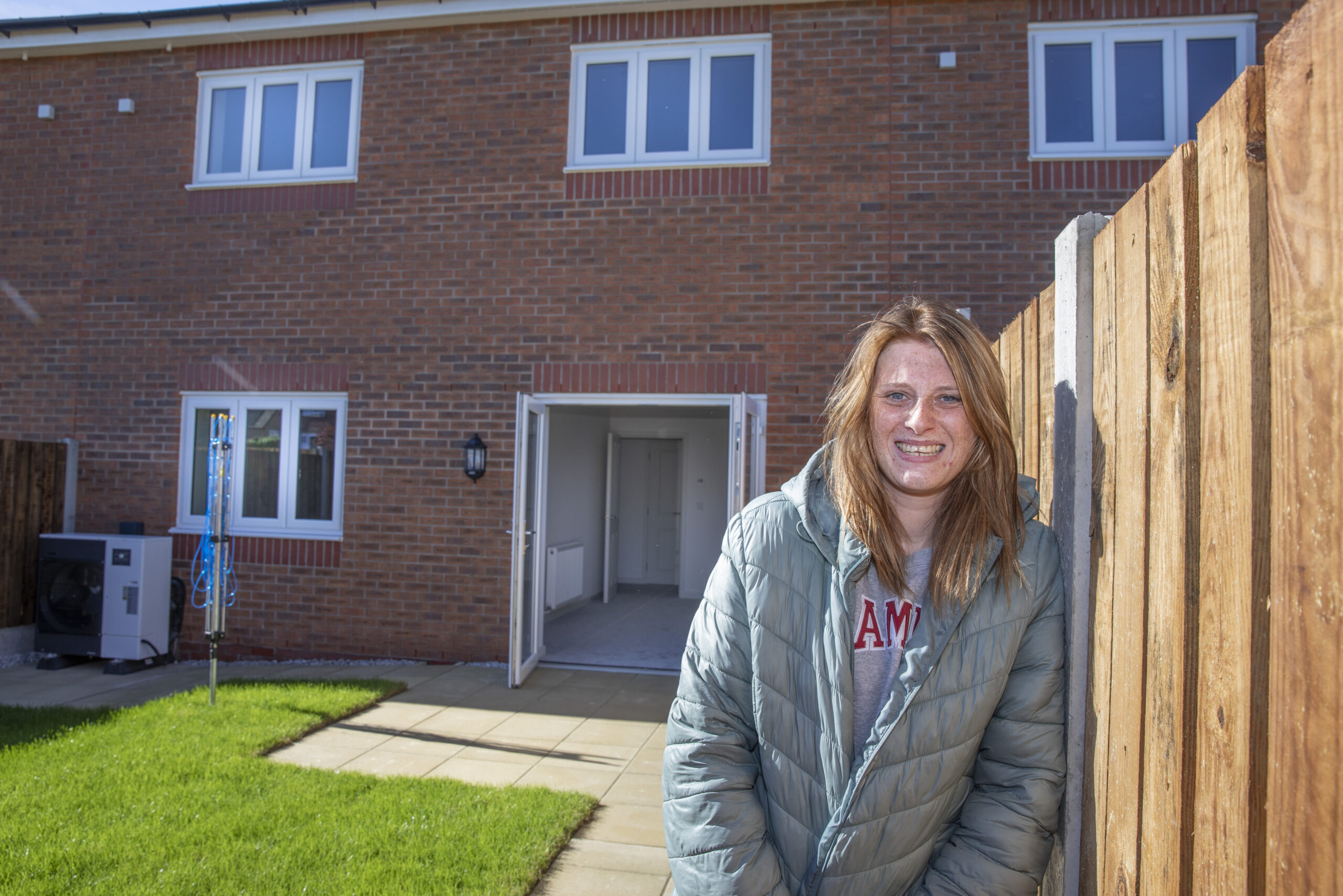 A woman stands outside a red brick home smiling